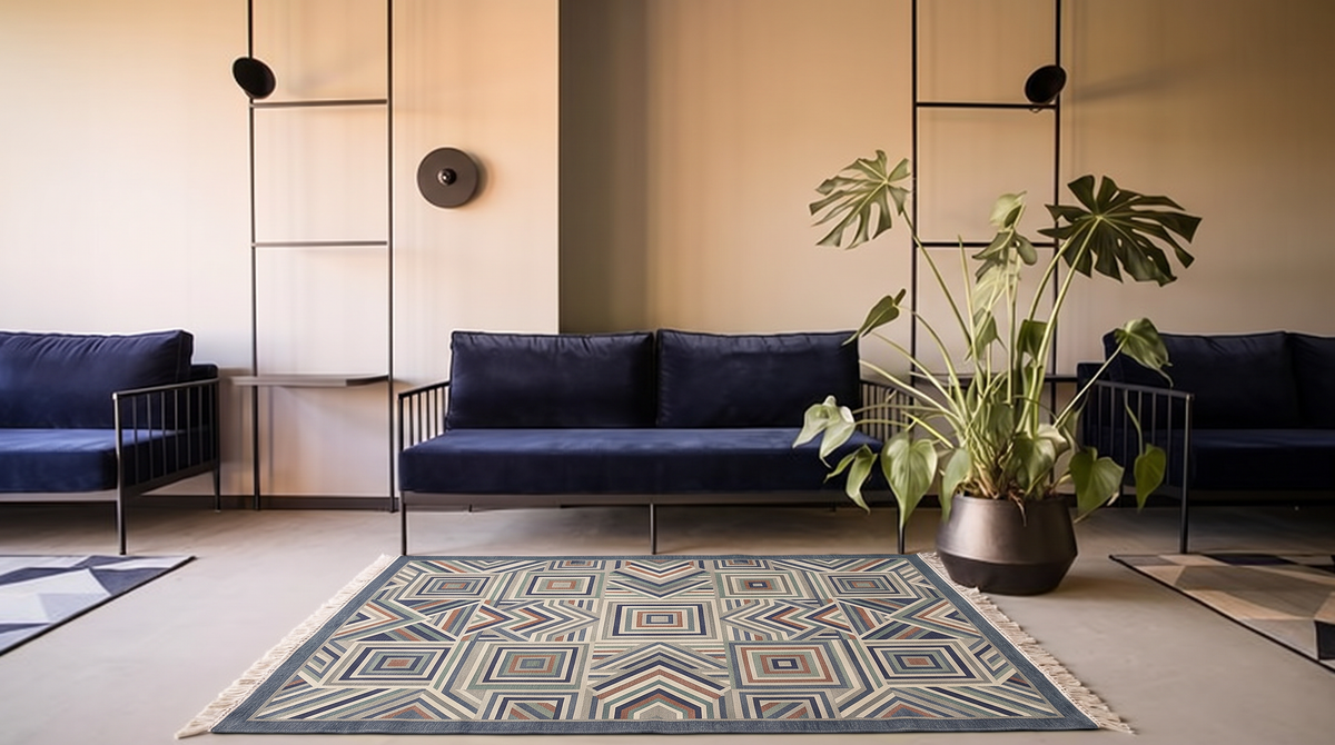 Slate-bordered hand-tufted wool rug with concentric squares and chevrons in slate blue, sage, rust and ivory, in a room with a navy sofa and a potted plant